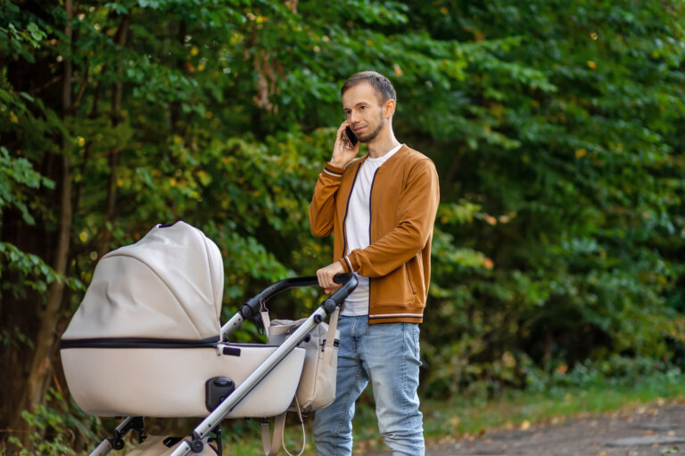 Man talking on mobile phone and pushing stroller in ma outdoors. Father on paternity leave.