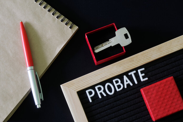 The inscription probate on a black board next to a notepad, pen and key in a red gift box. The concept of unexpected inheritance and memory of the testator. Close-up