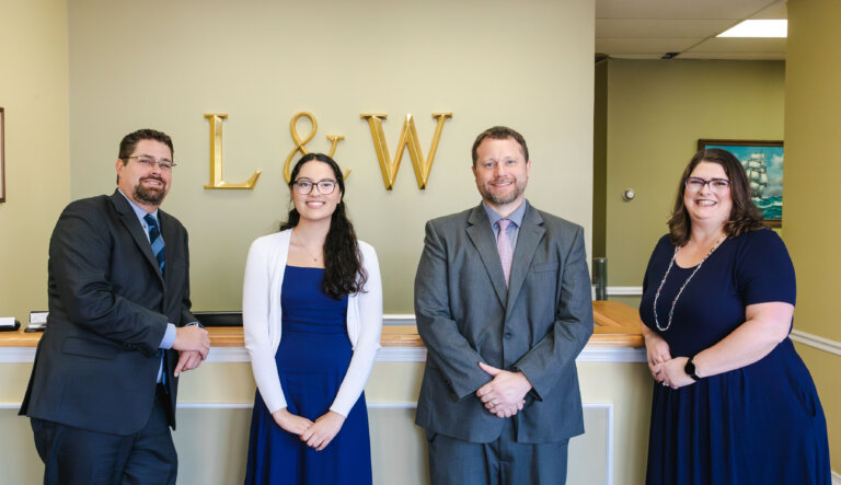 “Four attorneys and staff posing in front of firm logo”