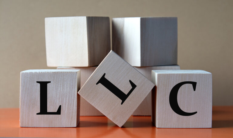 LLC (Limited Liability Company) - acronym on large wooden cubes on light brown background. Business concept