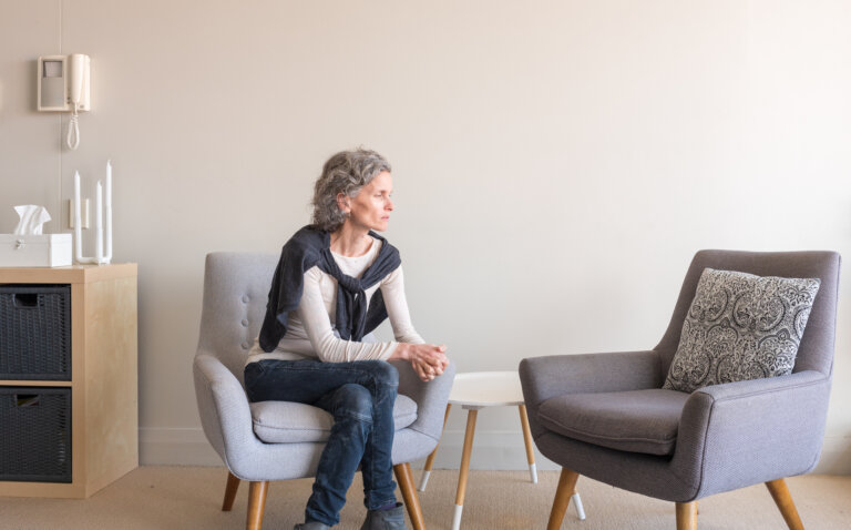 A woman sitting alone on a chair, looking thoughtful and pensive in a quiet room.