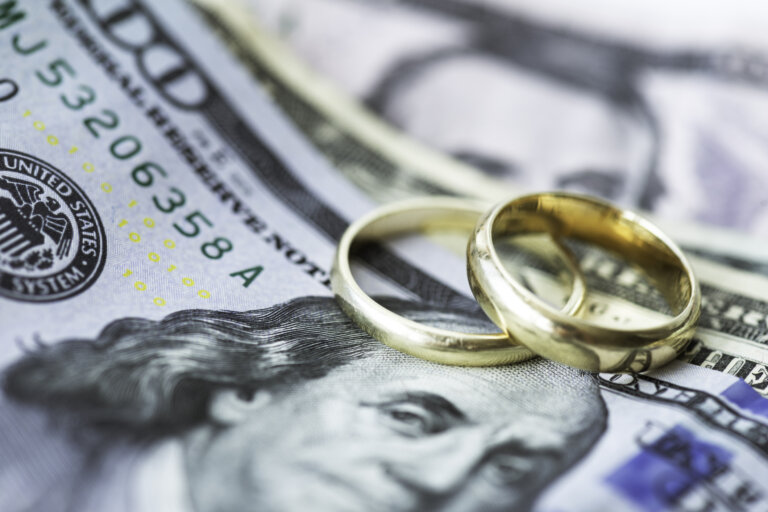 Two gold wedding rings placed on top of U.S. dollar bills.