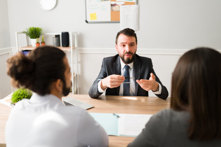 A lawyer in a suit speaking to a couple across a desk during a legal consultation.