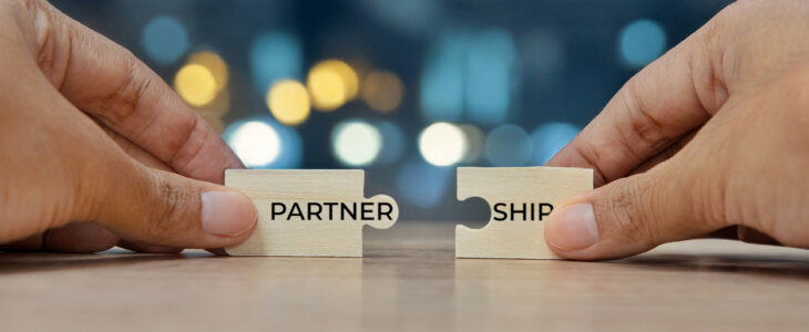 Two hands holding two puzzle pieces to form the word PARTNERSHIP. Collaboration and teamwork concept.