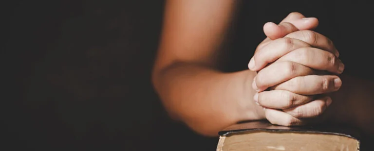 Hands clasped in prayer resting on a Bible