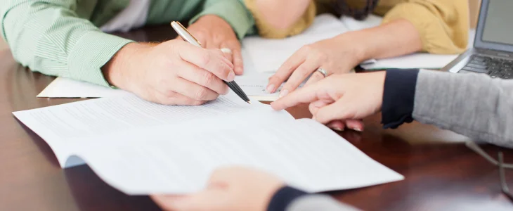 “Close-up of people reviewing and signing legal documents at a table.”