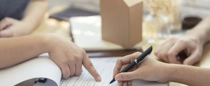 “Close-up of hands pointing and signing a contract document on a desk.”