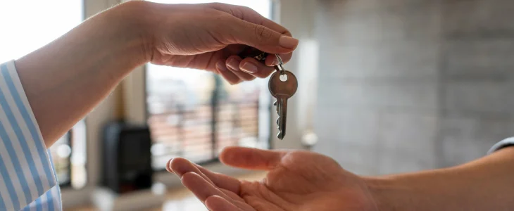 “Close-up of one person handing a house key to another.”