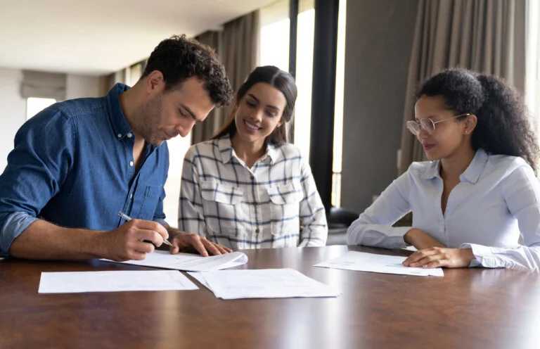 Happy Latin American couple buying a house and signing the deed in front of their real estate agent - home ownership concepts