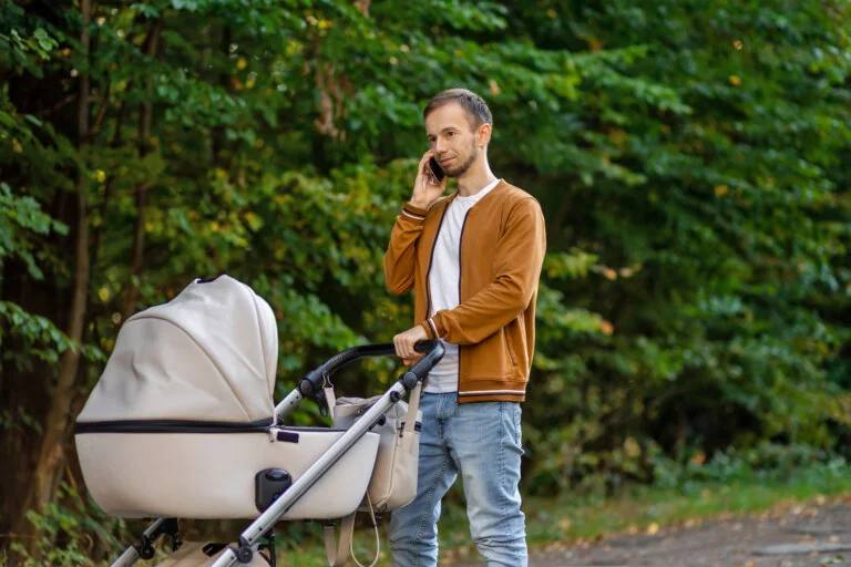 Man talking on mobile phone and pushing stroller in ma outdoors. Father on paternity leave.