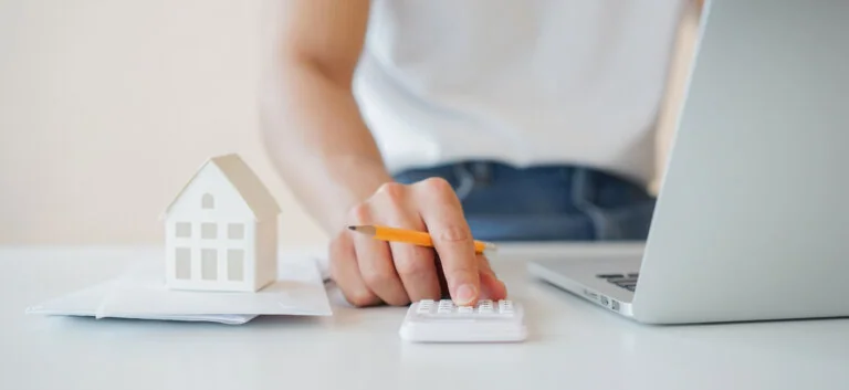 close up man hand counting on calculator with house's model on invoice letter to summary of refinance expense for planning and manage money about home loan mortgage and interest rates for people lifestyle concept